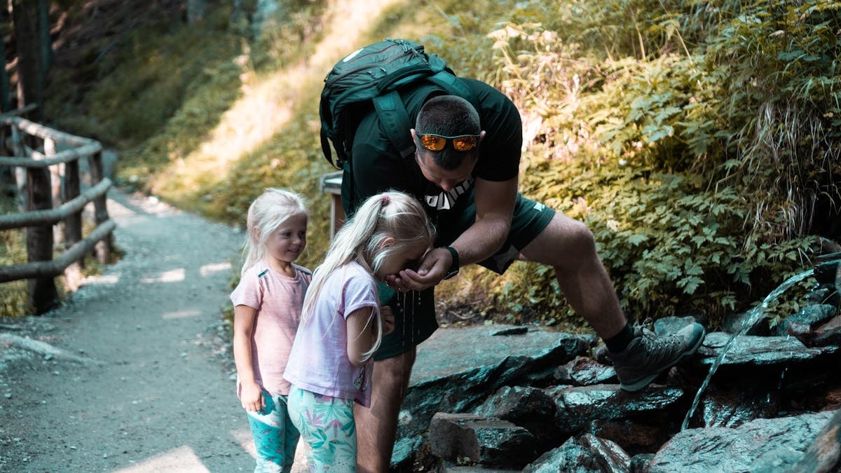 Father with daughters exploring nature on a forest path during a hike.